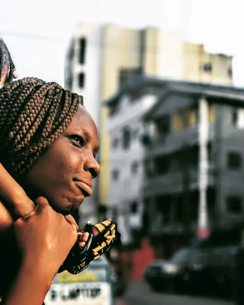A mother carrying her young daughter on her shoulders on a city street in Lagos, Nigeria.