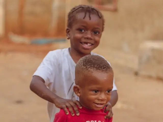 Two toddlers running and smiling outdoors in Abuja, Nigeria.
