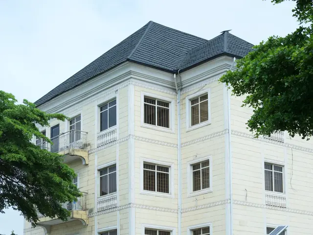 A white apartment block with a grey roof and cars parked by its gate, in Abuja, Nigeria.