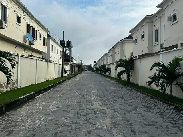 A paved estate street lined with walls, white houses and palm trees in Ajah, Lagos.