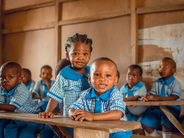 Young pupils in blue and white checked uniforms sitting at wooden desks in a classroom in Nigeria.