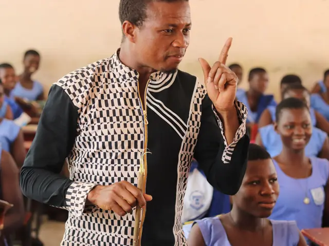 A teacher in a patterned shirt explaining a point to pupils in blue uniforms in a classroom in Wa, Ghana.
